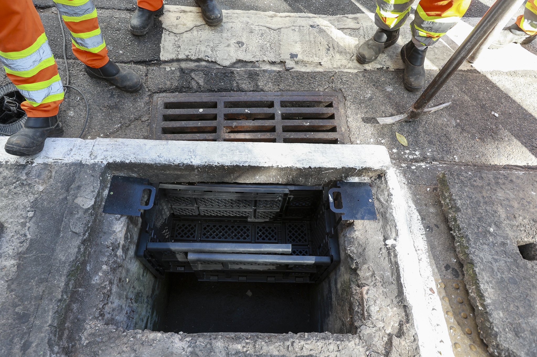 Bueiro aberto na rua, nocentro a imagem mostra um dispositivo plástico encaixado dentro do bueiro que serve como uma peneira  para o lixo  carregado pela água da chuva.