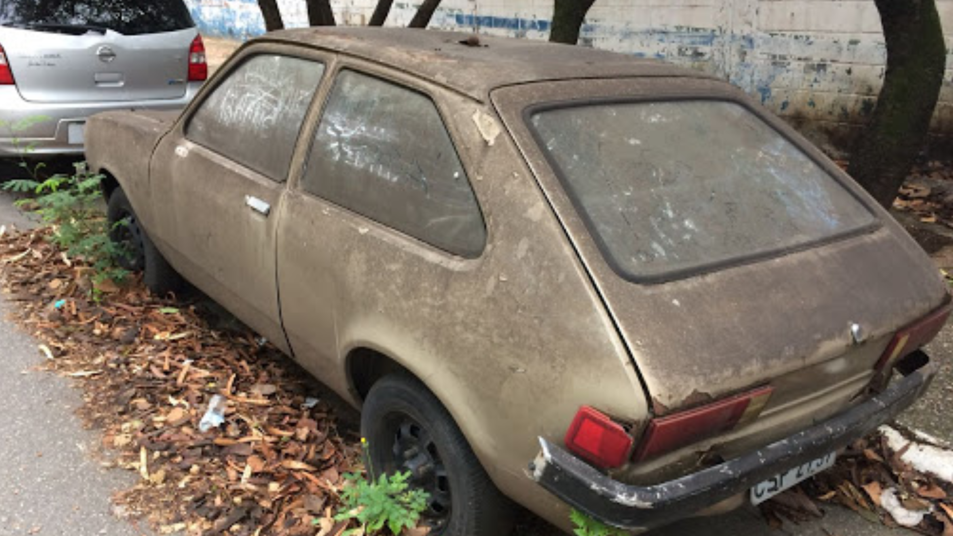 Carro marrom sujo e quebrado abandonado na rua.