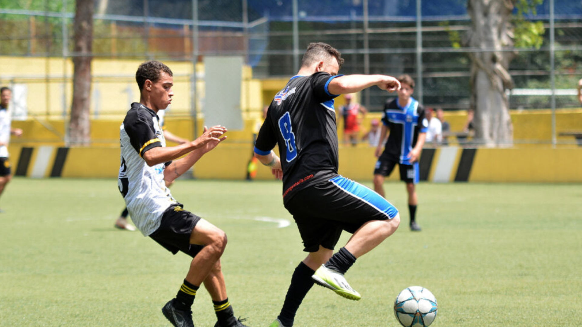 Duas pessoas jogando disputando o domínio da bola em um campo de futebol. 